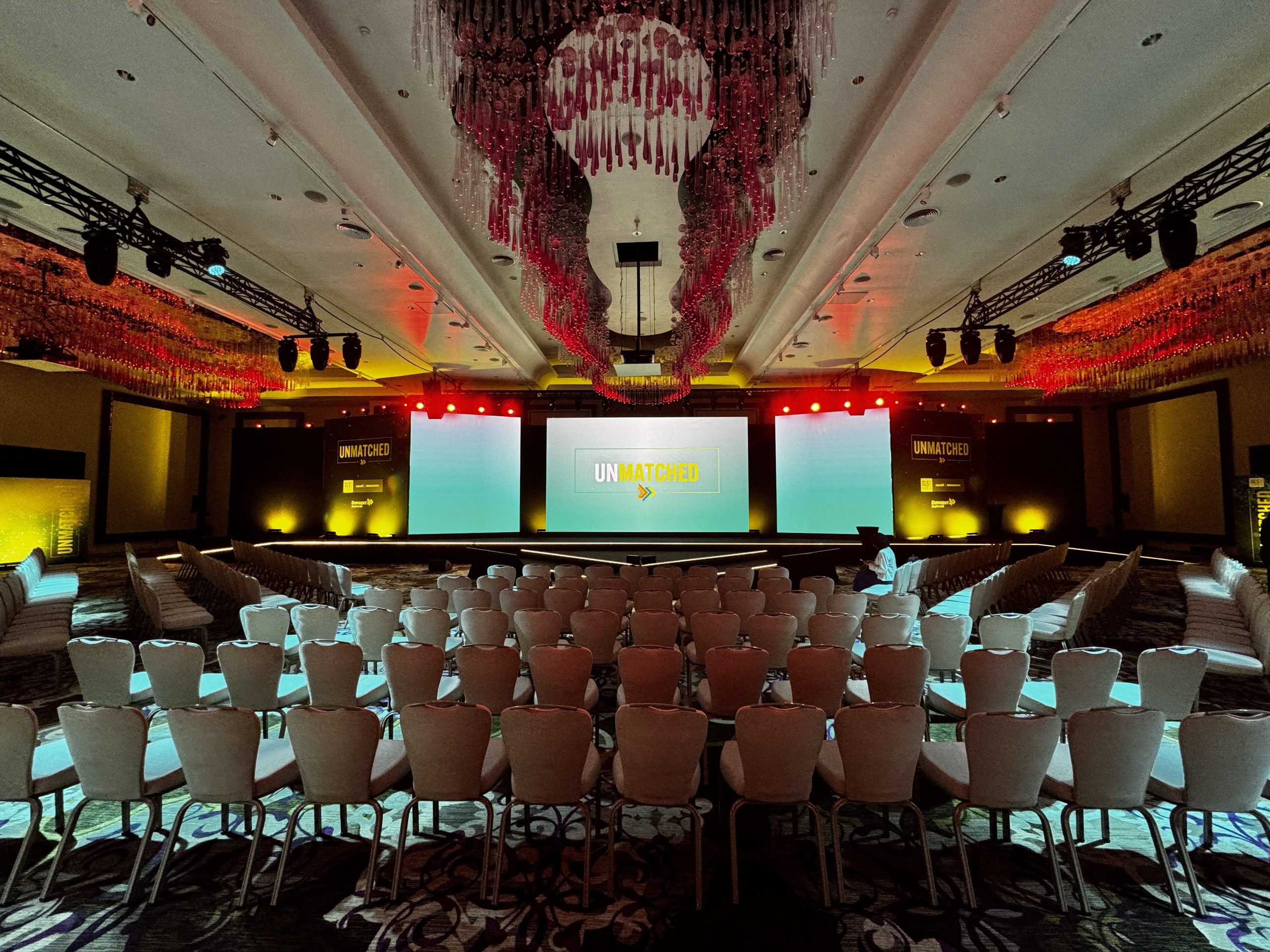 Zakelijk congres met groot videoscherm, podiumverlichting en publiek tijdens een presentatie.
